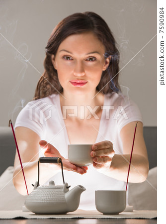 Young woman sitting in meditation pose in front of tea set and a Young woman sitting in meditation pose in front of tea set and a 7590984