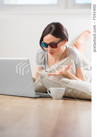 A young woman lying on the floor in front of her laptop with cup A young woman lying on the floor in front of her laptop with cup 7591400
