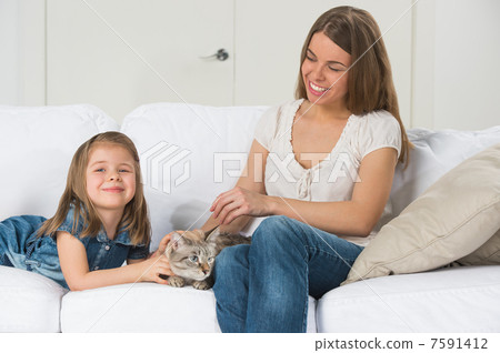 Mother and daughter sitting on sofa and cuddling cat Mother and daughter sitting on sofa and cuddling cat 7591412