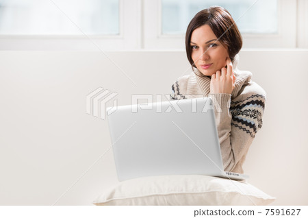 A young woman sitting on the floor in front of her laptop, looki A young woman sitting on the floor in front of her laptop, looki 7591627