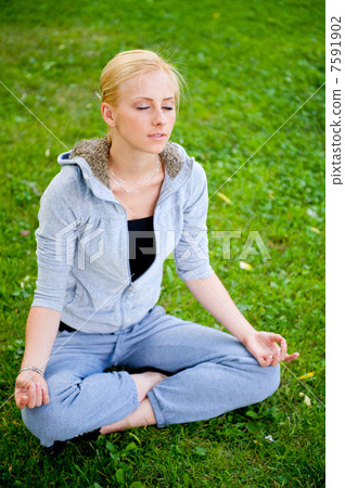 Portrait of young woman meditating in pose of lotus on green gra 7591902