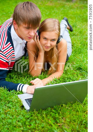 Happy young couple using laptop while lying on grass 7591905