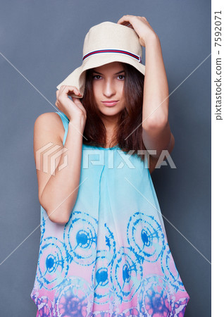 Confident woman with arms near her head holding hat against a bl 7592071