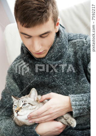Relaxed man sitting on armchair holding and petting pet cat 7592217