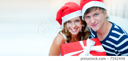 Portrait of young pretty couple standing indoors wearing Santa C 7592448