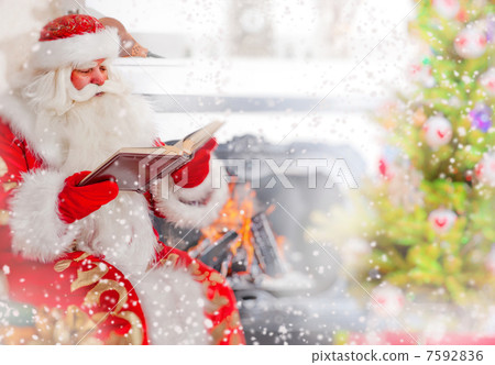 Santa sitting at the Christmas tree, near fireplace and reading Santa sitting at the Christmas tree, near fireplace and reading 7592836