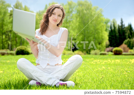 Young woman with laptop sitting on green grass 7594872