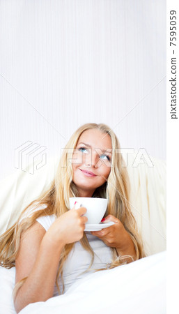 Smiling woman drinking a coffee lying on a bed at home or hotel. 7595059