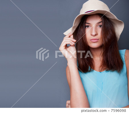 Confident woman with arms near her head holding hat against a bl 7596098