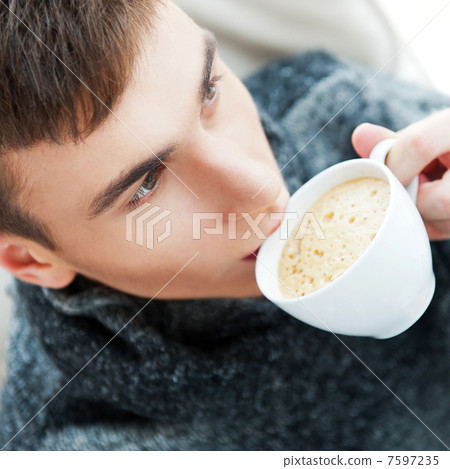 Portrait of a young man drinking coffee while sitting on armchai 7597235