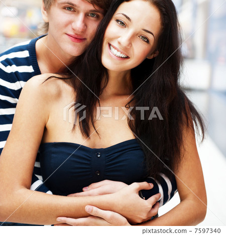 Portrait of young couple embracing at shopping mall and looking 7597340