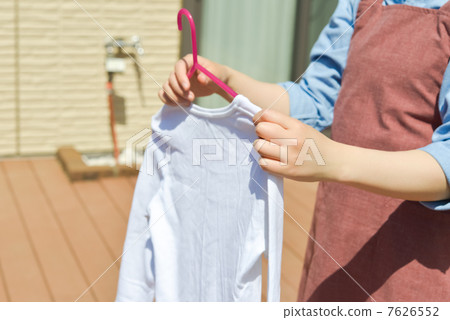 A woman in an apron hangs a shirt on the balcony to dry. A woman in an apron hangs a shirt on the balcony to dry. 7626552