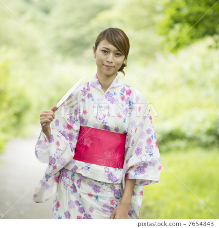 A woman in a yukata wearing a fan and smiling A woman in a yukata wearing a fan and smiling 7654843