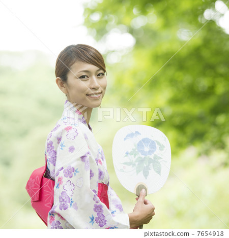 A woman in a yukata wearing a fan and smiling 7654918