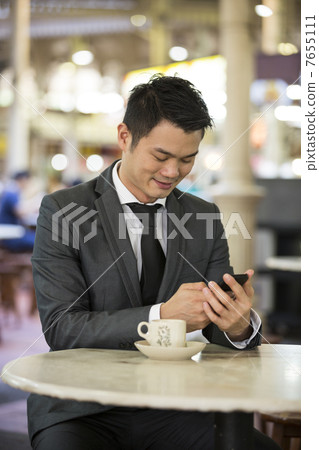 Chinese business man in a food court using his phone. Chinese business man in a food court using his phone. 7655111