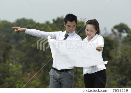 Asian couple standing outside looking at Architects drawings. Asian couple standing outside looking at Architects drawings. 7655319