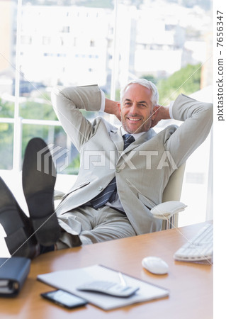 Businessman relaxing at his desk and smiling at camera 7656347