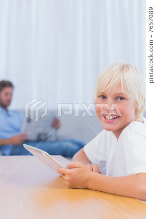 Boy using tablet with his father reading a book on the couch 7657089