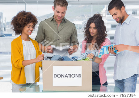Happy team of volunteers taking out clothes from a donation box 7657394