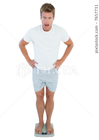 Shocked man standing on a weighing scale 7657731