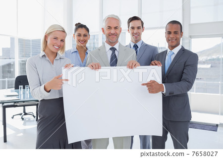 Business team holding large blank poster and pointing to it 7658027
