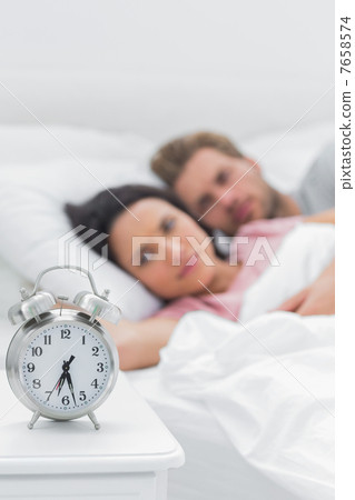 Couple lying in their bed next to an alarm clock Couple lying in their bed next to an alarm clock 7658574
