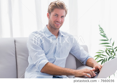 Man using his laptop sat on the couch 7660036