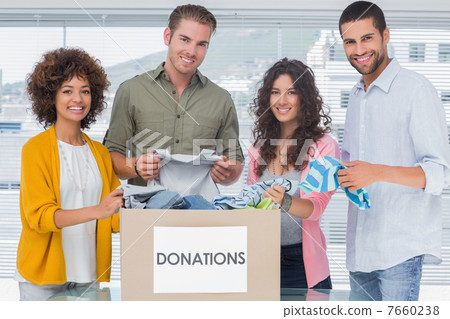 Smiling team of volunteers taking out clothes from a donation bo 7660238