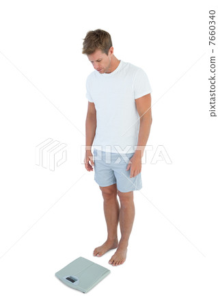 Athletic man looking at a weighing scale 7660340