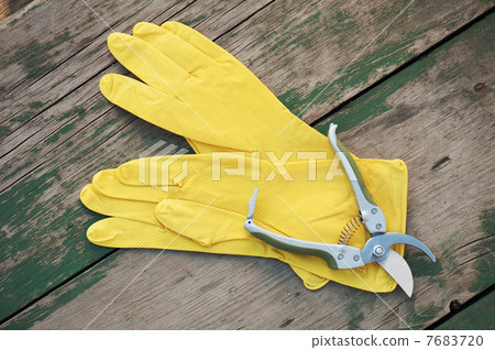 Yellow rubber gloves and garden pruner on wooden background. 7683720