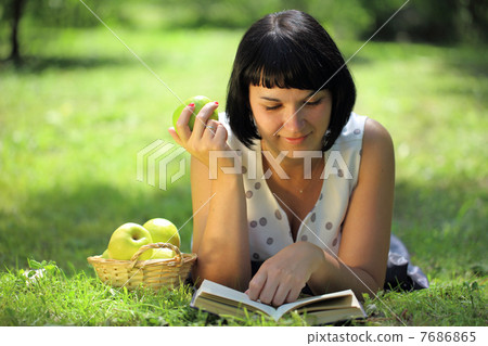 Young woman holding apple and reading book on grass Young woman holding apple and reading book on grass 7686865