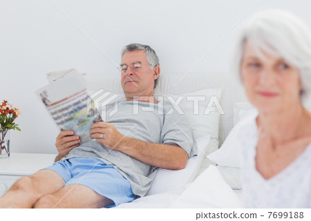 Mature man reading a newspaper in bed Mature man reading a newspaper in bed 7699188
