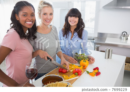 Cheerful friends preparing a meal together looking at camera Cheerful friends preparing a meal together looking at camera 7699229