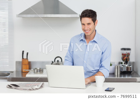 Portrait of a man using a laptop in the kitchen Portrait of a man using a laptop in the kitchen 7699511