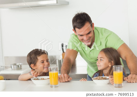 Father chatting to his children while they are having breakfast Father chatting to his children while they are having breakfast 7699513
