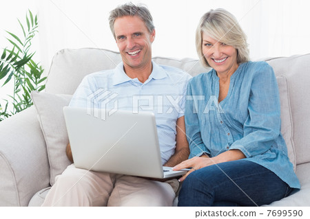 Happy couple using laptop together on the couch looking at camer 7699590