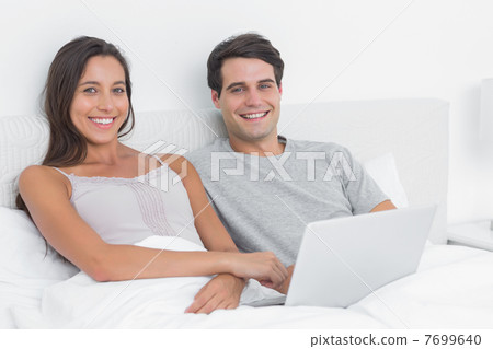 Portrait of a couple using a laptop together lying in bed Portrait of a couple using a laptop together lying in bed 7699640