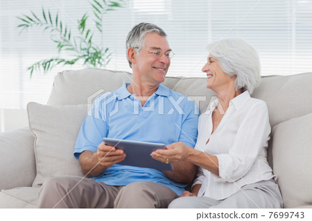 Couple using a tablet pc sitting on the couch Couple using a tablet pc sitting on the couch 7699743