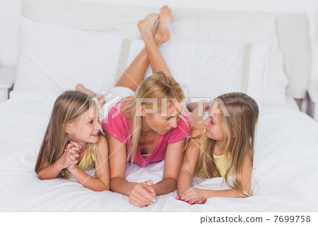 Twins relaxing with their mother in bed 7699758