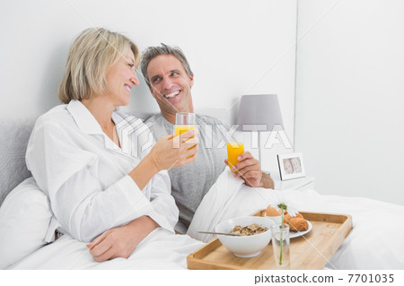 Cheerful couple having orange juice at breakfast in bed 7701035