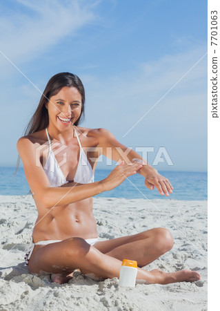Happy woman sitting on beach applying sunscreen Happy woman sitting on beach applying sunscreen 7701063