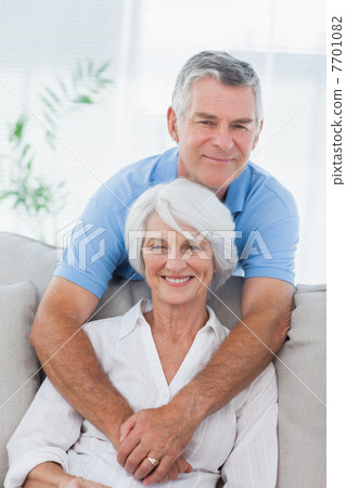 Man hugging his wife who is sitting on the couch 7701082