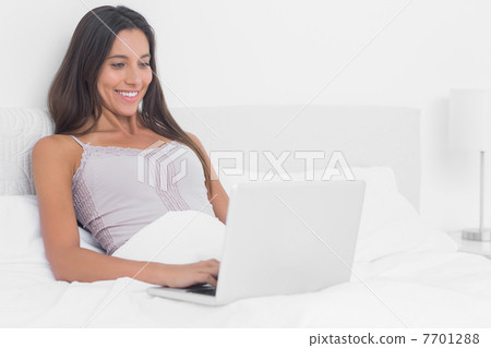 Woman using her laptop in bed 7701288