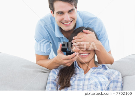 Man hiding his girlfriends eyes and offering her an engagement r Man hiding his girlfriends eyes and offering her an engagement r 7702100