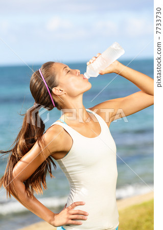Fitness woman drinking water after beach running Fitness woman drinking water after beach running 7733730