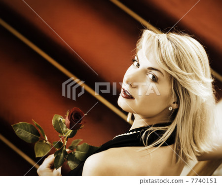 Beautiful young woman standing on a red carpet and holding a ros 7740151