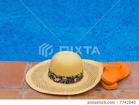 straw hat and sandals by pool side 7742040