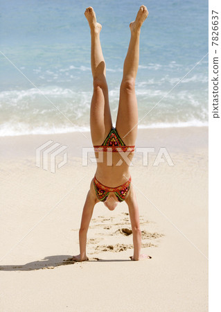 Young woman headstanding on the beach 7826637