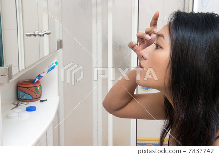 Woman looking at her reflection in the mirror Woman looking at her reflection in the mirror 7837742