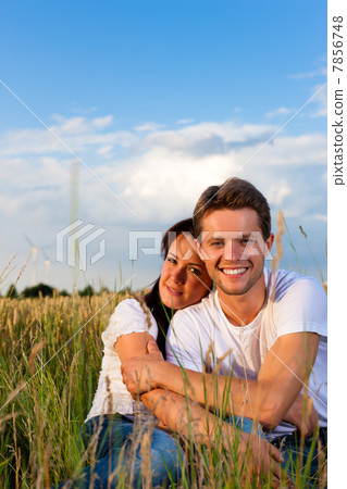 Happy couple sitting on a meadow or grainfield Happy couple sitting on a meadow or grainfield 7856748
